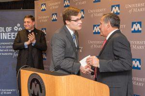 ​​​​​​​University of Mary Student Chris Riedman receives scholarship from ETP’s Chris Curia, Mary President Monsignor James Shea claps in background.