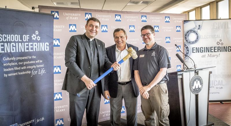 Monsignor Shea, Chris Curia and Dr. Terry Pilling standing with a sledge hammer