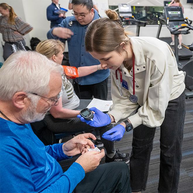 Students checking an elderly man's blood sugar.