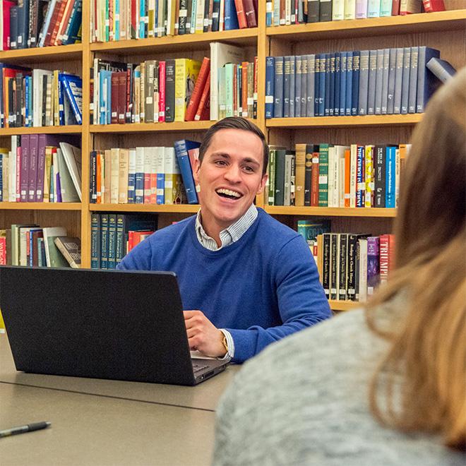 students sitting at a table with a professor discussing a religious book.