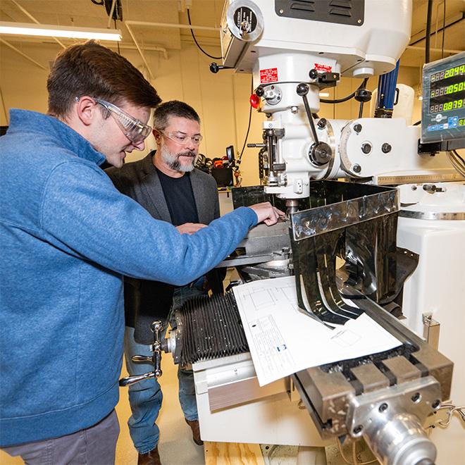 Engineering student asking professor a question while using machinery.