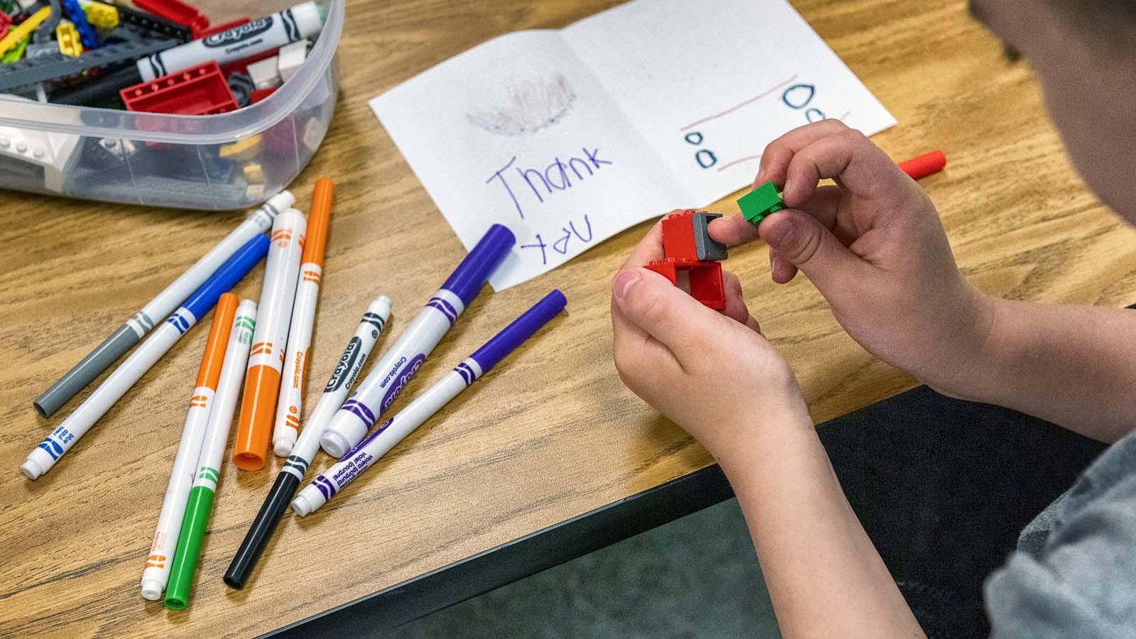 Young child playing with legos with markers and coloring sheet on table