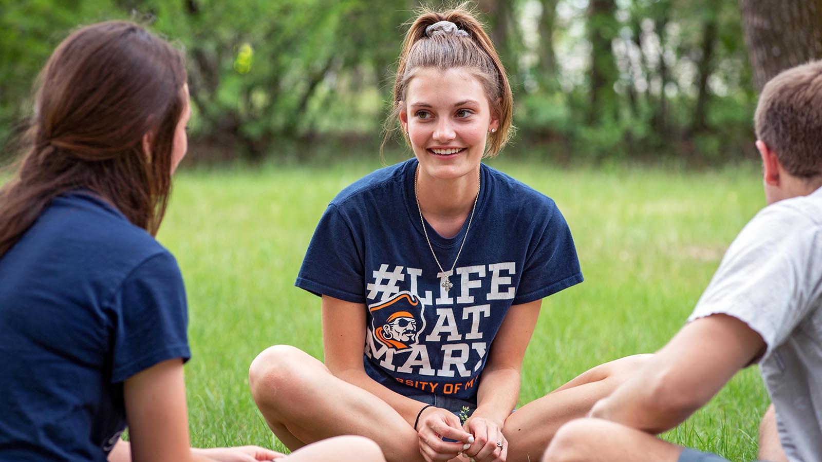 Three students sitting in the grass having a conversation.