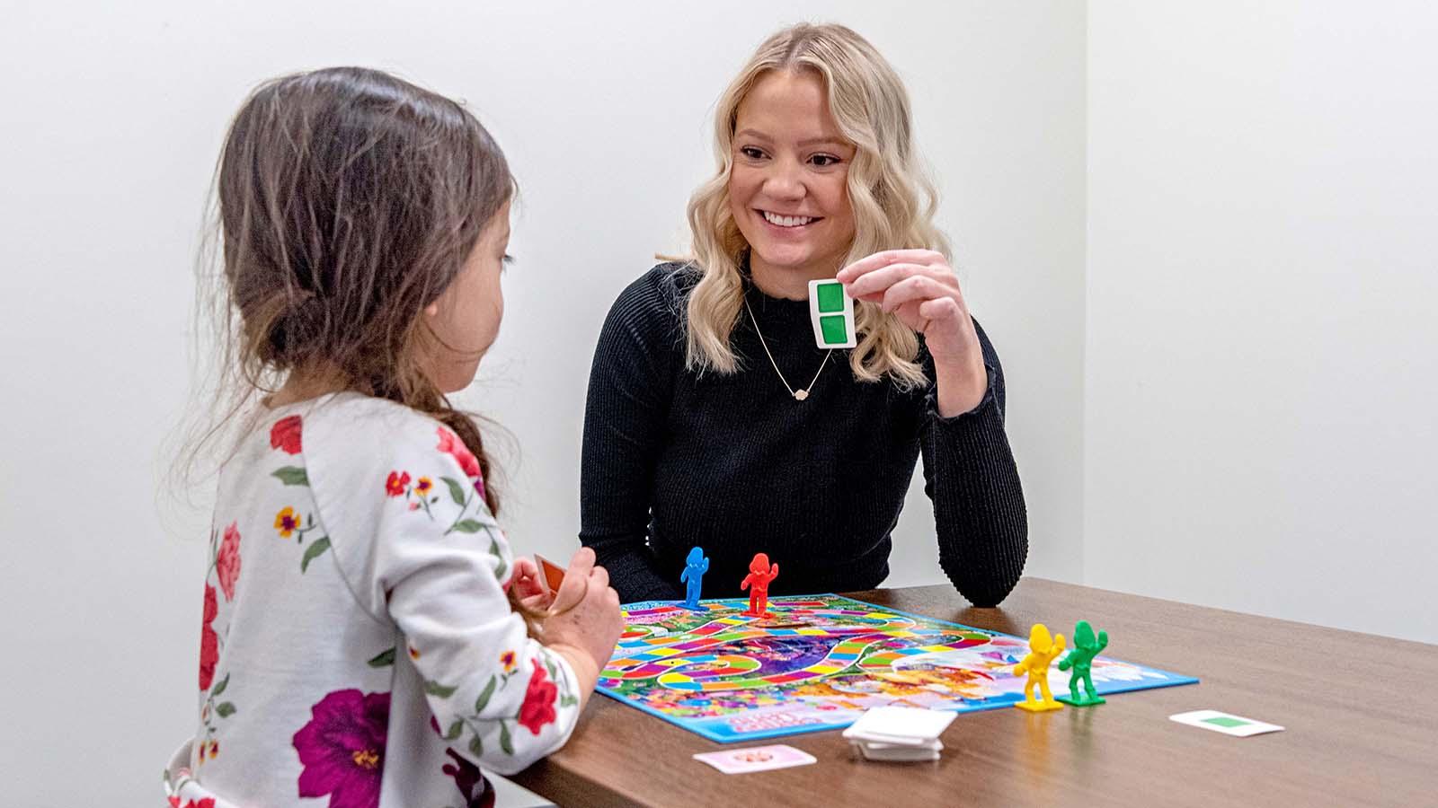 College student playing board game with young girl