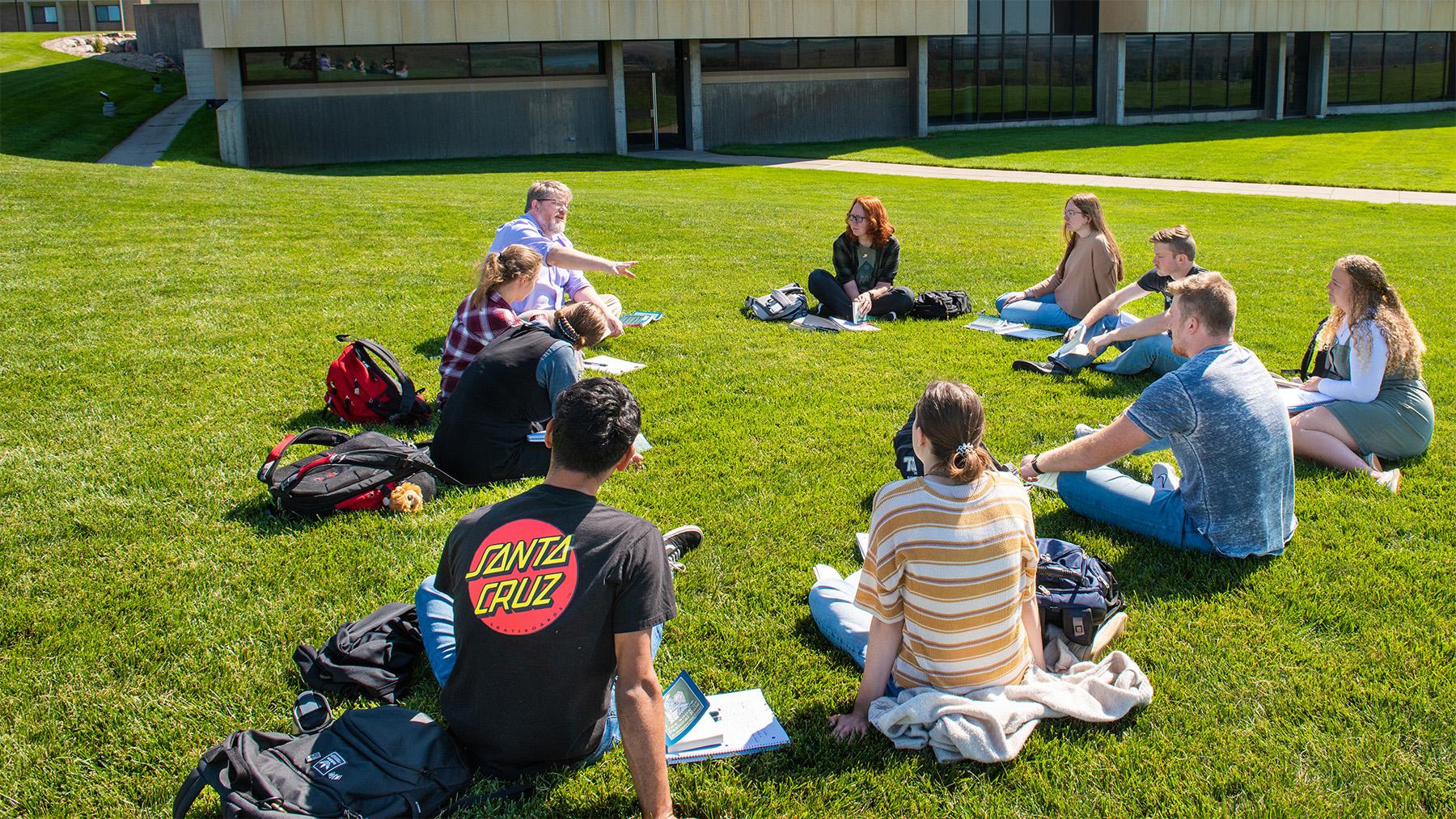 A professor teaching a class outside on the lawn.