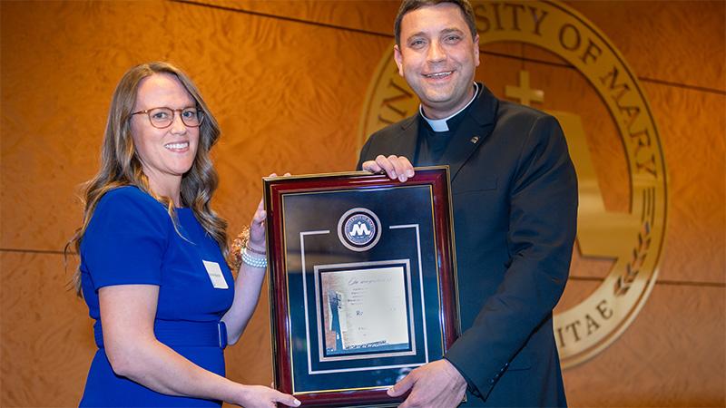 Monsignor with an alumni holding an award plaque