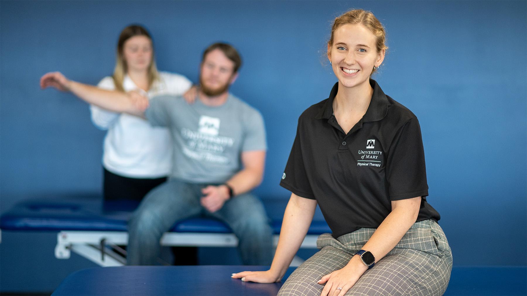 Student sitting in the forefront with a physical therapist working in the background.